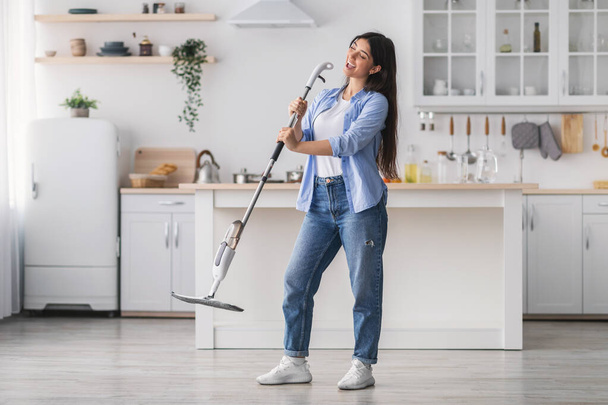 Mujer alegre limpieza piso cantando celebración fregona en cocina - Foto, imagen