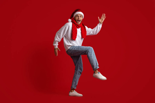 Świąteczny taniec. Zabawny facet w Santa kapelusz taniec nad czerwonym tle Studio - Zdjęcie, obraz