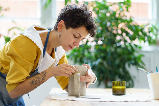 Jonge beeldhouwer meisje maken keramische servies in de studio. Vrouw aardewerk kunstenaar werk met natte klei - Foto, afbeelding