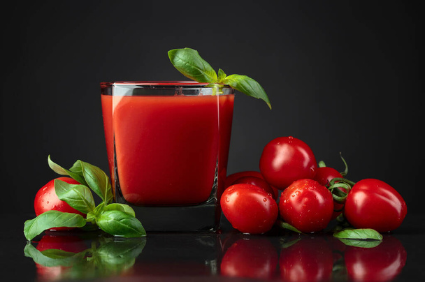 Tomato juice and wet tomatoes with green basil on black table. - Photo, Image