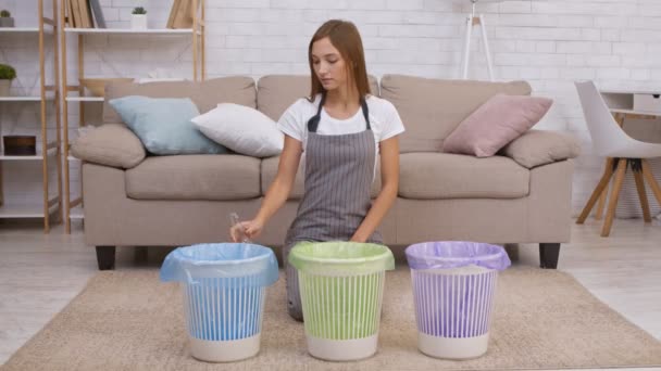 Nuori positiivinen kotiäiti laittaa lasipullon siniseen roskakoriin kotona, tukee ympäristönsuojelua - Materiaali, video