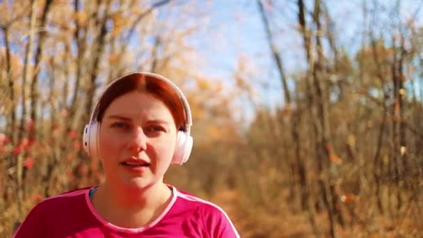 Actieve gerunde vrouw met witte koptelefoon draait in de natuur autimn vallen. Fitness concept voor gezonde levensstijl. - Video