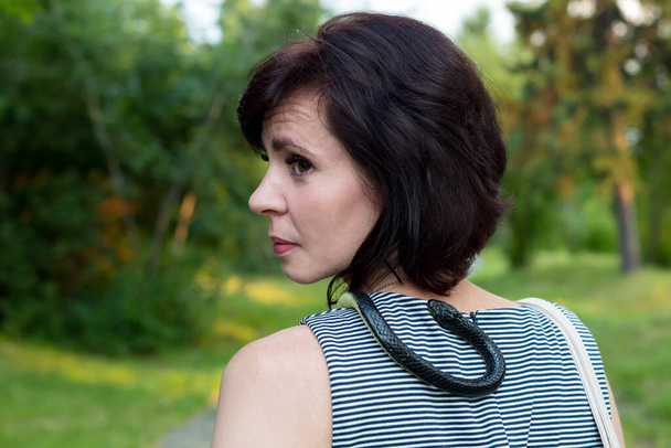 A woman with a live snake around her neck walks through the park. - Fotoğraf, Görsel
