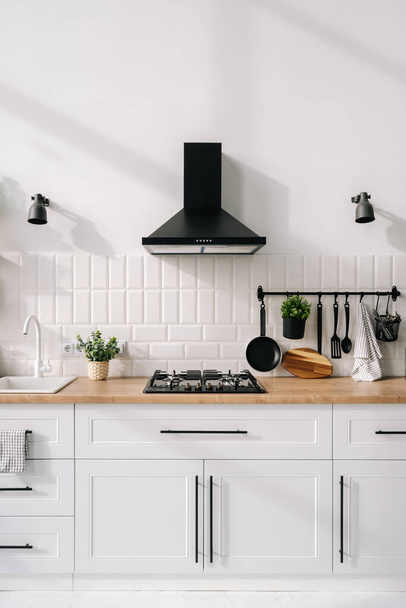 Сучасний дизайн інтер'єру кухні в білих тонах з кухонною плитою, раковиною, капюшоном і технікою. Дерев'яна меблева концепція. Квартира класу люкс в оренду. Новий комфортний будинок
 - Фото, зображення