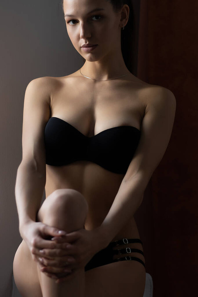 Smyslná štíhlá mladá žena nosí černé spodní prádlo odhalující tělo křivky dotýkající se hlavy, zatímco stojí u zdi - Fotografie, Obrázek
