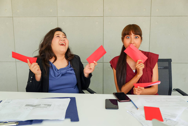 Deux jeunes femmes asiatiques reçoivent un bonus ou un salaire ou de l'argent avec une enveloppe rouge est heureusement, concept de nouvelle année chinoise - Photo, image