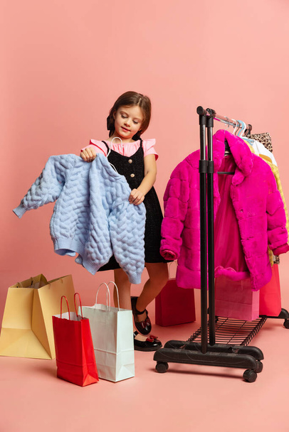Beautiful little girl, cute kid choosing outfit, dress in clothing store. Wow emotions, black friday, purchases, discount, ad. - 写真・画像