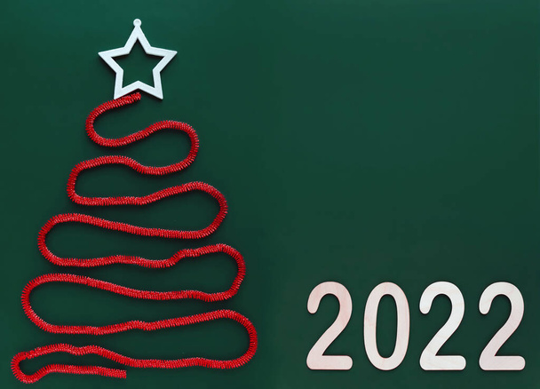 Creative Christmas tree made of red glittering tinsel, folded in a spiral on the left side with a white vault at the top, in the right corner the date of the new coming year number 2022, copy space. - Foto, Imagem