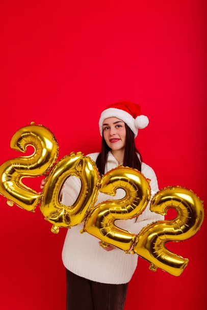 Buone Feste - una giovane donna con un cappello rosso di Natale tiene i numeri 2022 - Foto, immagini