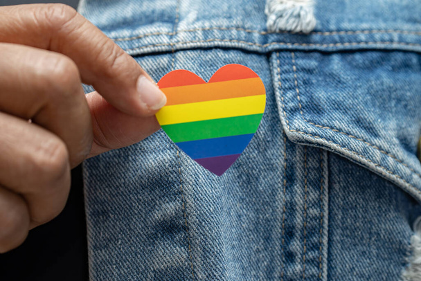 Ázsiai hölgy visel kék farmerdzseki vagy farmer ing és gazdaság szivárvány színű zászló szív, szimbóluma LMBT büszkeség hónap ünneplik éves júniusban a meleg, leszbikus, biszexuális, transznemű, emberi jogok. - Fotó, kép