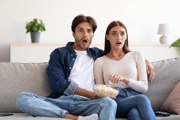 Yllättynyt pelästynyt nuori eurooppalainen pari, jolla on avoin suu, syö popcornia ja katsoo elokuvaa - Valokuva, kuva