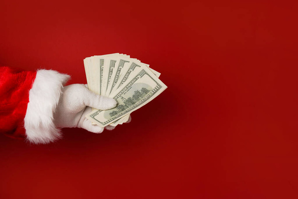 Άγιος Βασίλης χέρι κρατώντας χρήματα σε κόκκινο φόντο, αντίγραφο χώρο - Φωτογραφία, εικόνα