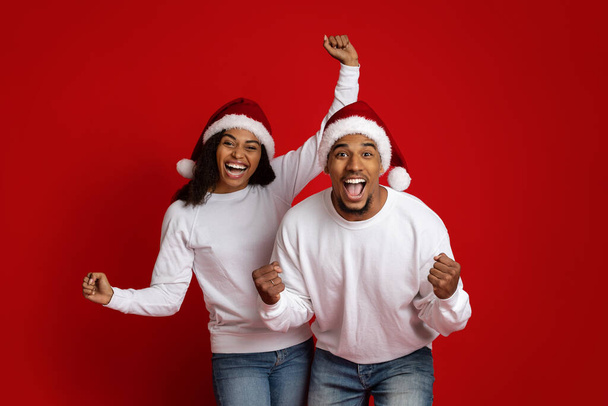 Emotional black couple in Santa hats gesturing on red - Foto, Imagen