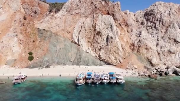 Drone tiro de las montañas volcánicas de color naranja de la isla de Suluada y la playa blanca con turistas y yates en la bahía - Metraje, vídeo