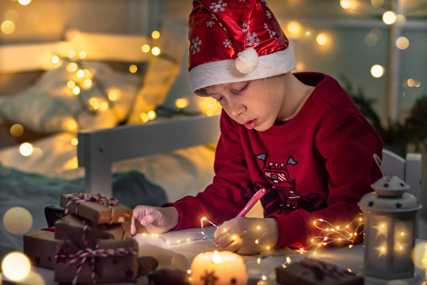 Рождественская традиция мальчик в красной кепке пишет письмо с пожеланиями Санта-Клаусу - Фото, изображение