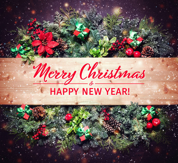 Плоская зимняя рождественская композиция с еловыми ветвями, ягодами, шишками, цветами пуансеттии и подарочными коробками на тёмном фоне. Текст с Рождеством и Новым годом - Фото, изображение
