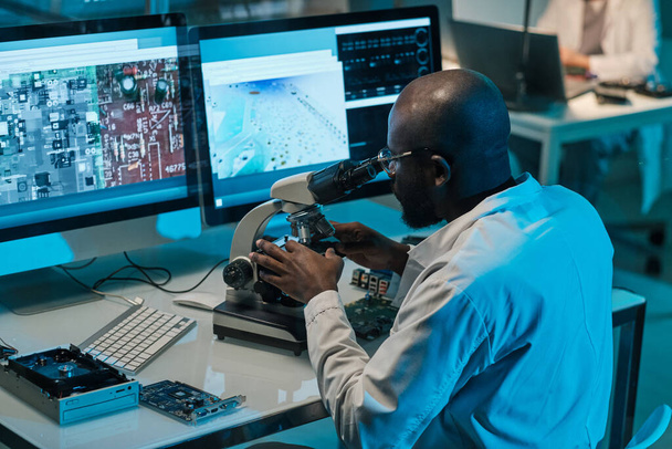 Αφρικανός επιστήμονας με μικροσκόπιο που εργάζεται μπροστά σε οθόνες υπολογιστών - Φωτογραφία, εικόνα