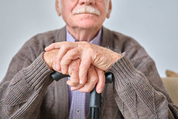 Oudere man zittend met kruk - Foto, afbeelding