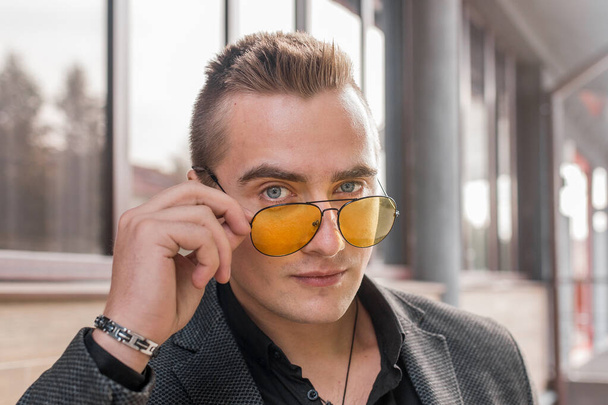 Portrait of a handsome man of European appearance businessman adjusting sunglasses with his hand, close-up on the outdoor of the street. - Foto, Imagem