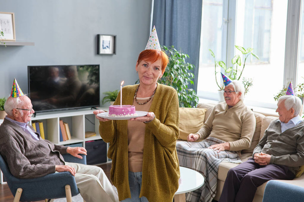 Пожилая женщина держит торт на день рождения - Фото, изображение