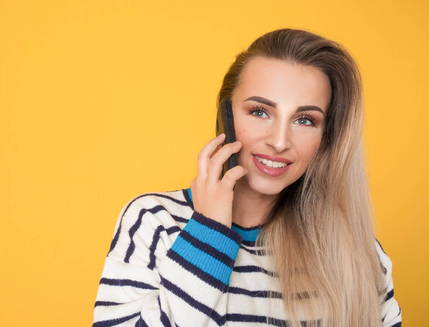 Happy young woman talks on the phone, isolated on yellow background. Female person using the smartphone. Studio shot - Foto, Imagem