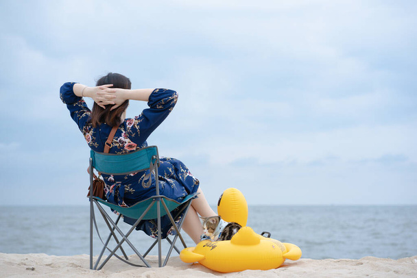 Kadın rahatla ve kedisiyle plaj sandalyesine otur. Plajda ördek kauçuğu halkasına otur. - Fotoğraf, Görsel