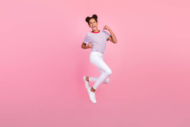 フルボディ写真のブルネットアフリカ系アメリカ人スタイリッシュな陽気な女の子身に着けているカジュアル衣装ジャンプ勝者隔離されたピンク色の背景 - 写真・画像