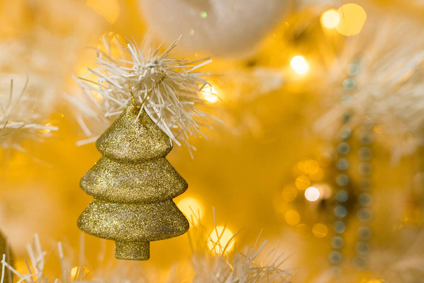 Großaufnahme von Goldbaumspielzeug und Girlanden auf weißgelbem Weihnachtsbaum - Foto, Bild