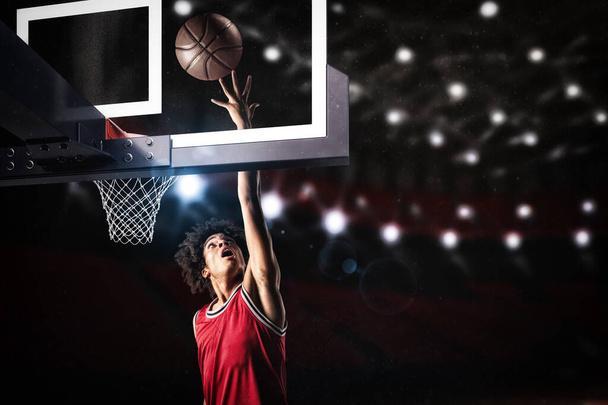 Basketball player in red uniform jumping high to make a slam dunk to the basket - Foto, afbeelding