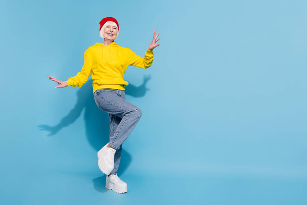 Full body photo of attractive funky old woman wear hat dance good mood isolated on blue color background - 写真・画像