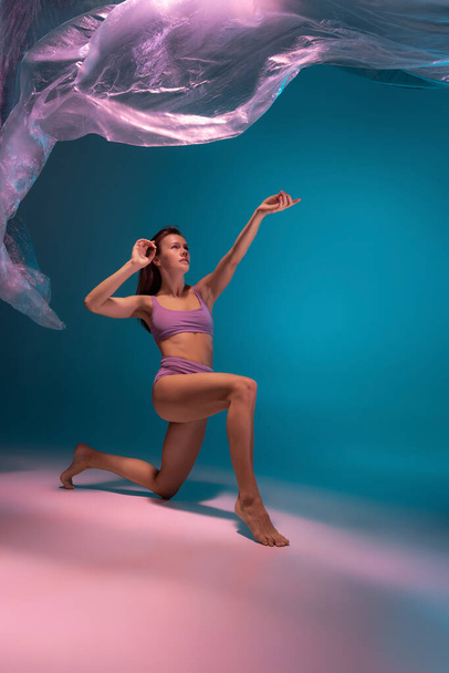 One young flexible contemp dancer dancing with fabric isolated on gradient blue white background in neon light - Foto, afbeelding