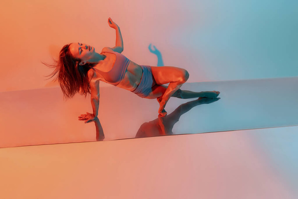 Young flexible, graceful girl, female contemp dancer in art performance isolated on gradient blue orange background in neon - Φωτογραφία, εικόνα