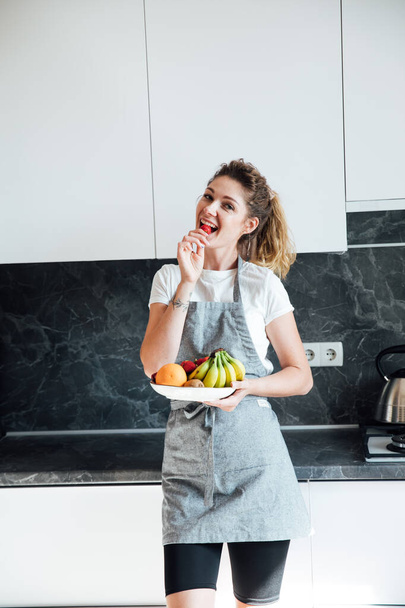 belle femme au foyer mange des fruits sucrés dans la cuisine - Photo, image