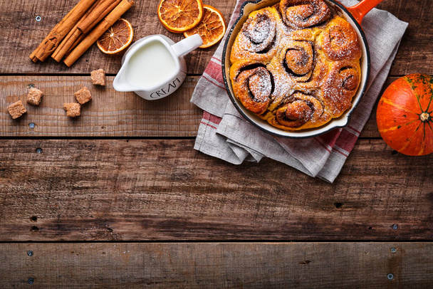 Cinnabon cinnamon rolls buns with pumpkin, nut, caramel and sugar cream iced on rustic wooden background table. Top view. Sweet Homemade Pastry christmas baking. Kanelbule - swedish dessert. - Photo, Image