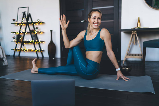 Europees meisje dat thuis yoga beoefent op een fitnessmat. Concept van een gezonde levensstijl. Jonge mooie glimlachende atletische vrouw in sportkleding kijkend naar de camera. Interieur studio appartement - Foto, afbeelding