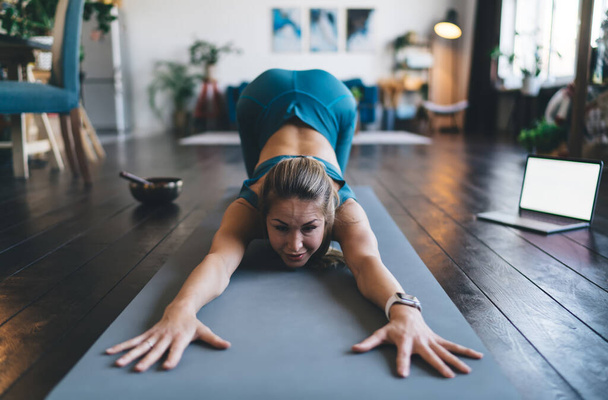 European girl practicing yoga on fitness mat at home. Young attractive athletic woman in sportswear and barefoot. Concept of healthy lifestyle. Interior of studio apartment - Foto, imagen