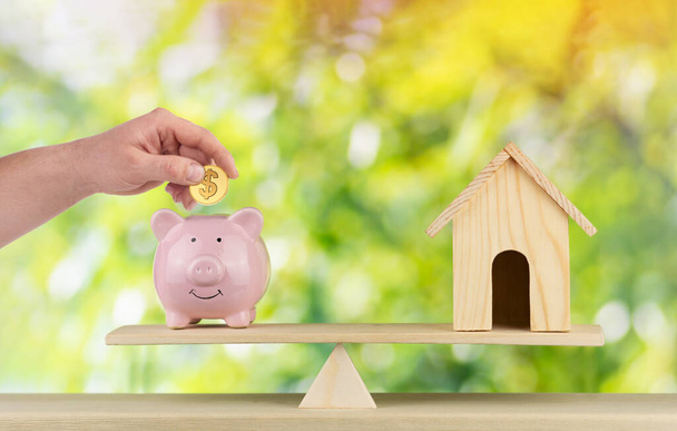 wooden home and piggy bank with hand hold gold coin Us dollar sign put on the scales with balance saving or loan for buy new house or plan business investment concept - Valokuva, kuva
