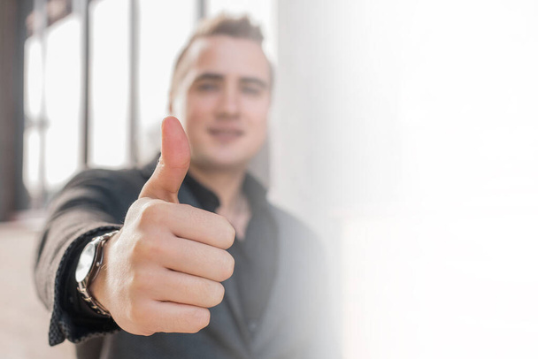 A young man shows a close-up of a thumbs up class against a street outdoor background. - Photo, Image