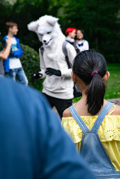 Une petite fille en salopette regarde le personnage poilu habillé comme un loup blanc ou un chien avec des gants. Défilé d'animes - Photo, image