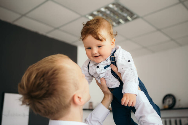 A kisfiú vigyorog vidáman aranyos gyermek vörös hajú nevető baba játszik az apjával hány fia. Toddler szórakozik otthon öltözött overál nadrágtartó és fehér ing. Boldog gyermekkort! - Fotó, kép