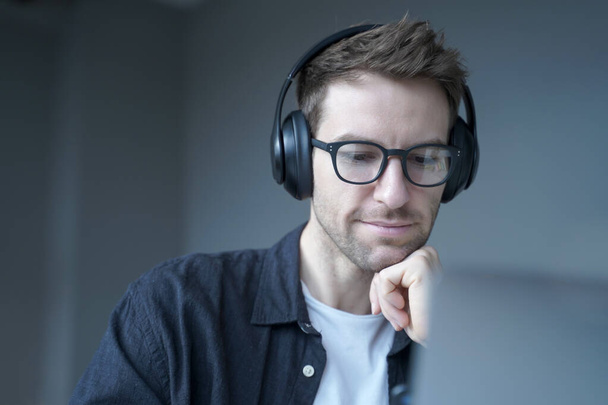 Homme allemand souriant dans les écouteurs regardant l'écran de l'ordinateur portable et regardant webinaire éducatif - Photo, image