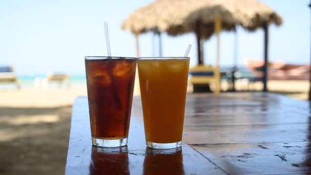 The photo shows Coca Cola refreshments and passion fruit juice. Photo taken in bar on a Caribbean island. The beach and ocean line are visible in the background.Refreshments are visible in foreground. - Fotoğraf, Görsel