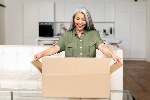 Excited positive middle-aged Asian woman opening cardboard box - Foto, imagen