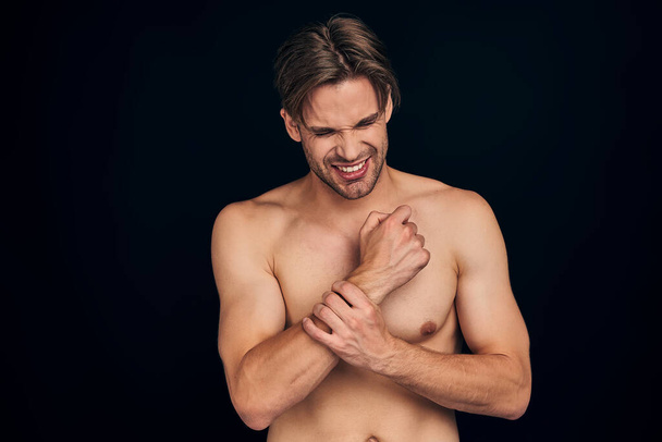 Handsome young bearded man isolated. Cropped image of topless muscular man is standing on black background. Man holding his wrist. Experiencing wrist pain. - Valokuva, kuva