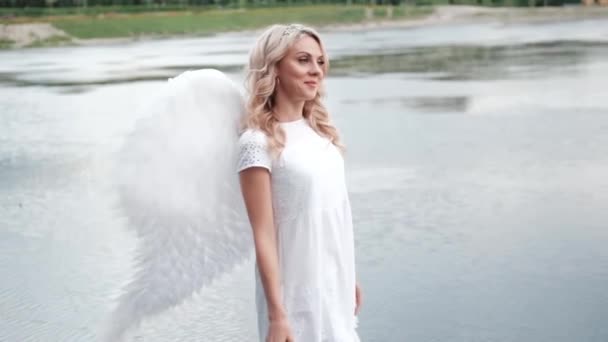 mooie engel in witte jurk. Geweldige blonde vrouw met lang krullend haar en witte vleugels. slow motion - Video
