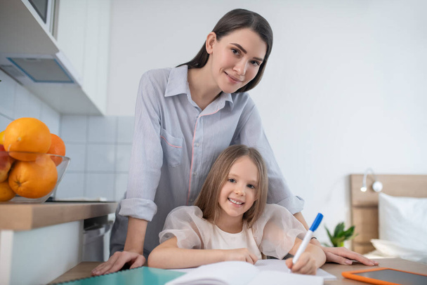 Kid doing homework aided by her mother - Фото, изображение