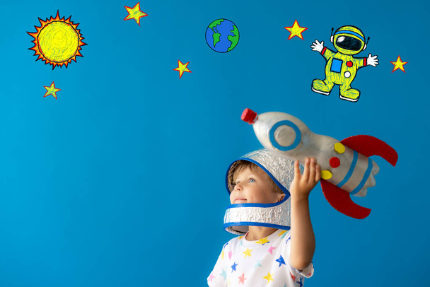 Happy child playing with toy rocket against blue background. Kid pretend to be astronaut. Imagination and children dream concept - Photo, Image