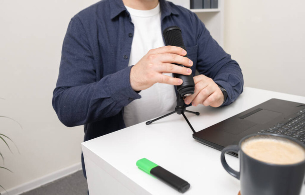 Un uomo con un microfono sta registrando un podcast mentre guarda nel suo portatile. Il concetto di blogging, apprendimento e comunicazione online. - Foto, immagini