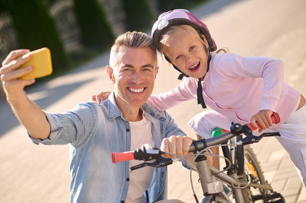 A smiling man making selfie with his kid on a bike - Foto, Imagem