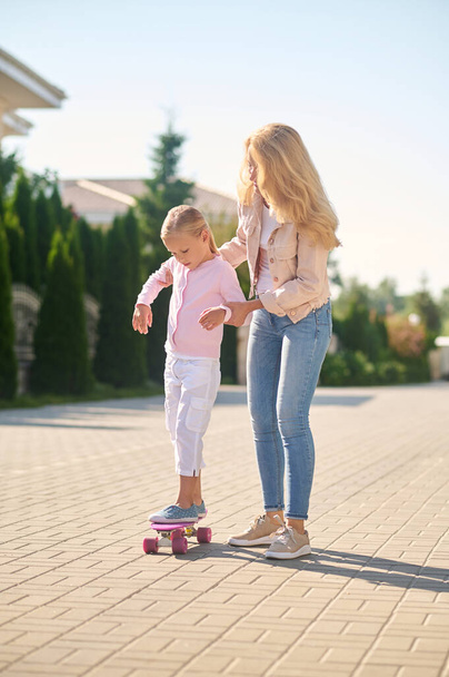 Mom helping her daughter ride a skateboard - Фото, зображення